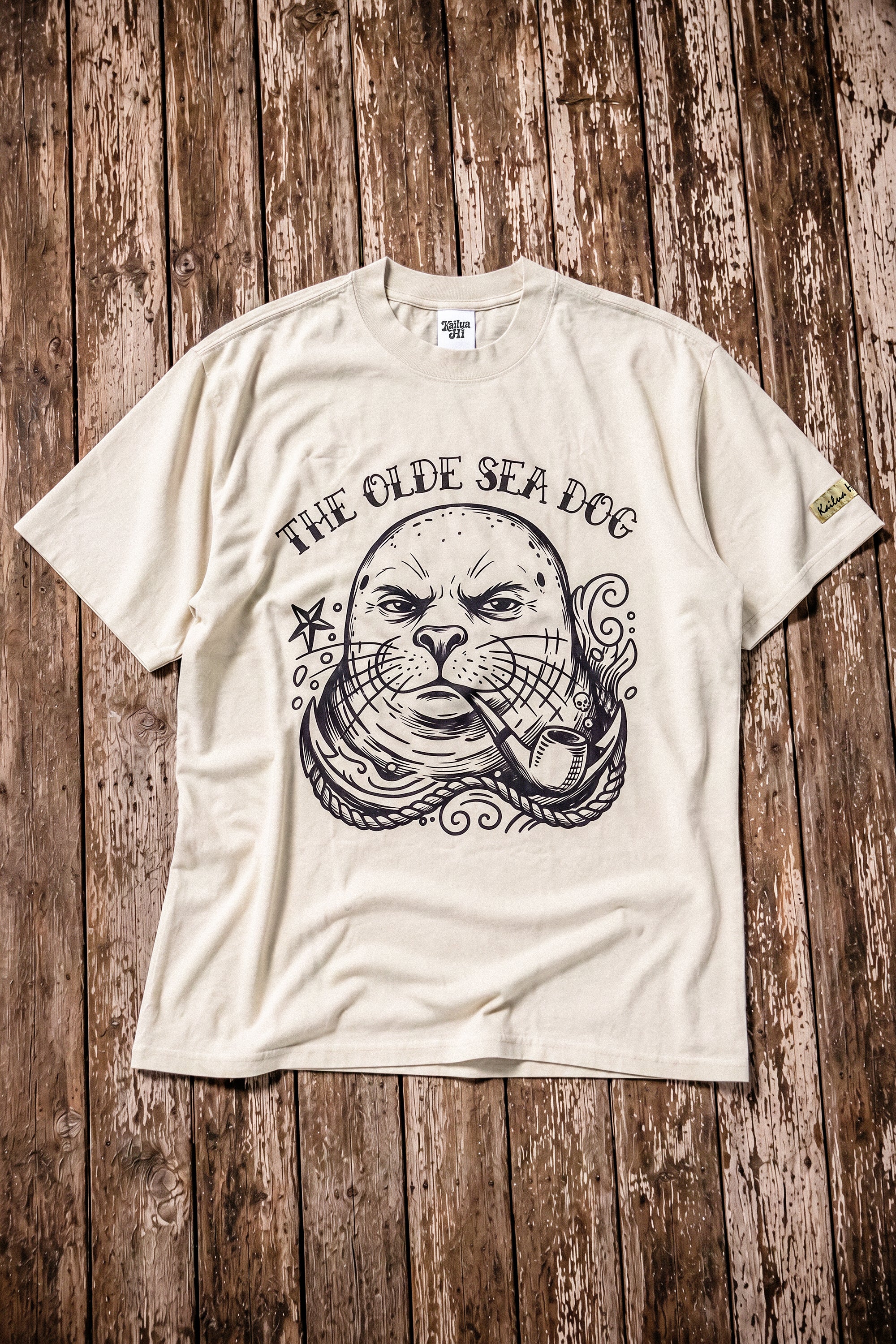 a faded green graphic tee with a monk seal design laying on a wood floor