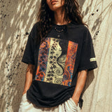woman wearing a black t-shirt with a colorful graphic design against a textured wall.