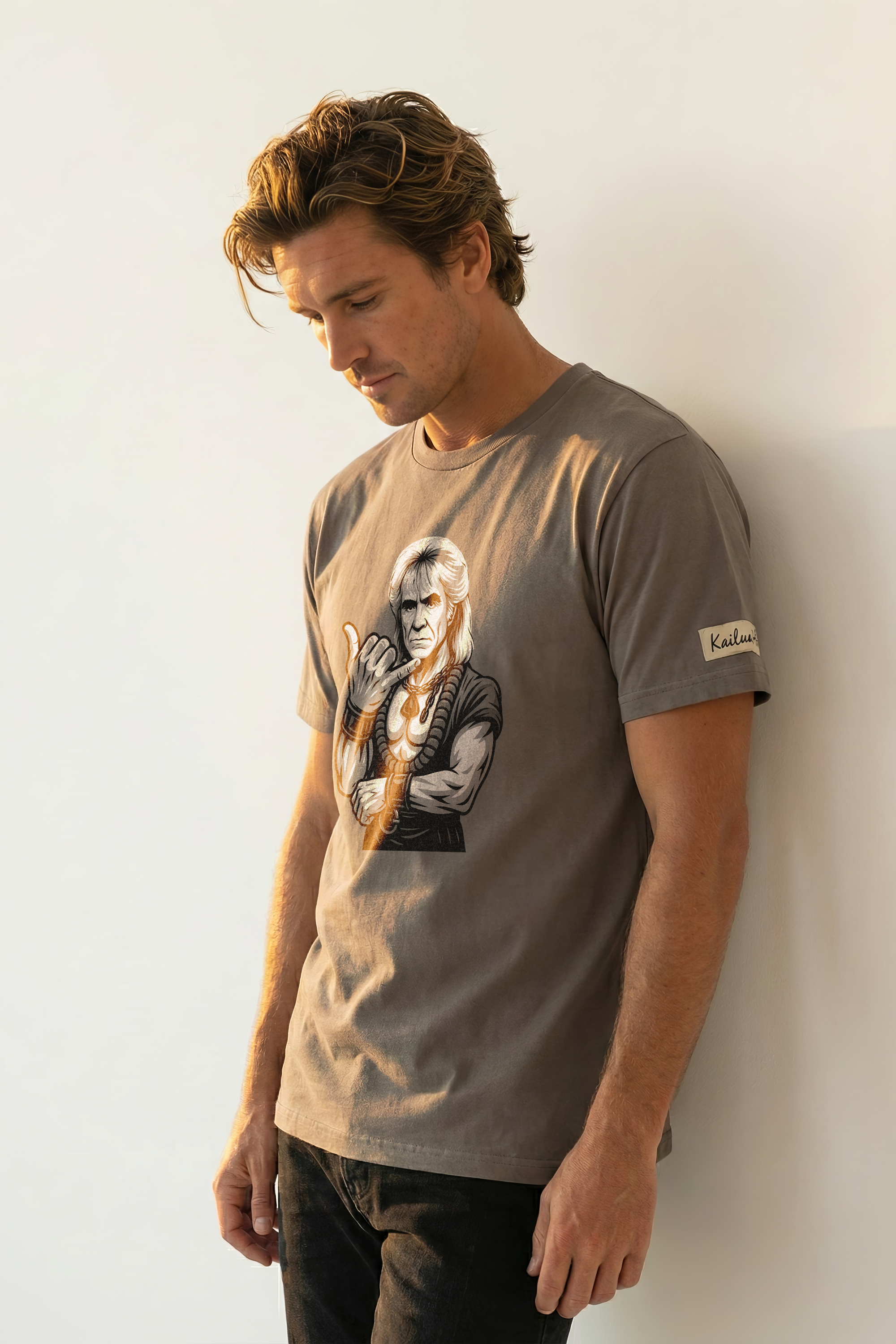 Man wearing a brown t-shirt with a graphic design of a man giving the shaka hand sign against a white wall