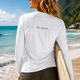 Woman holding a surfboard on a beach with 'be pono' shirt
