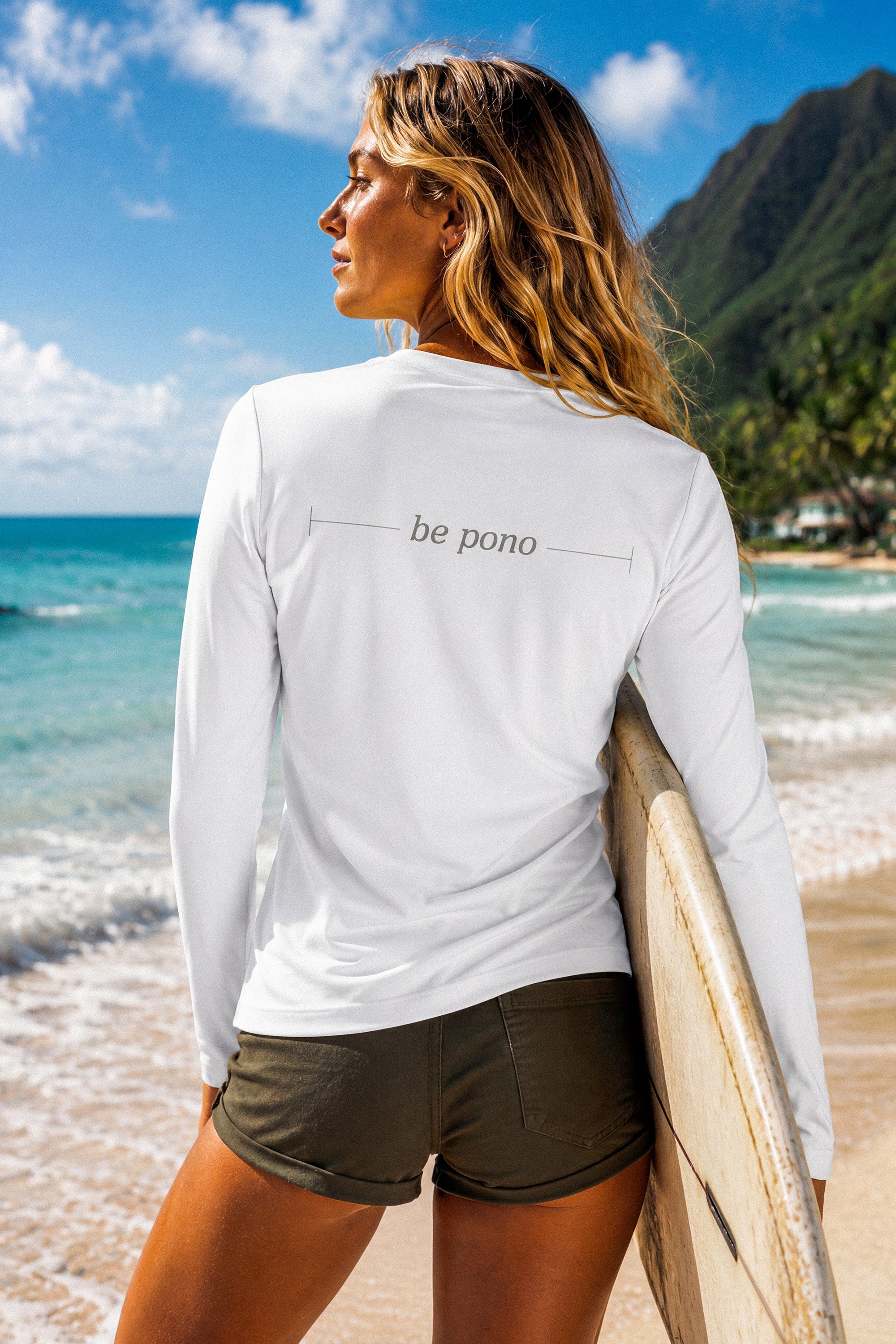 Woman holding a surfboard on a beach with 'be pono' shirt