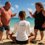 back view of woman seated on Kailua beach in white rash guard with “be pono” back print, tourists arguing beside her