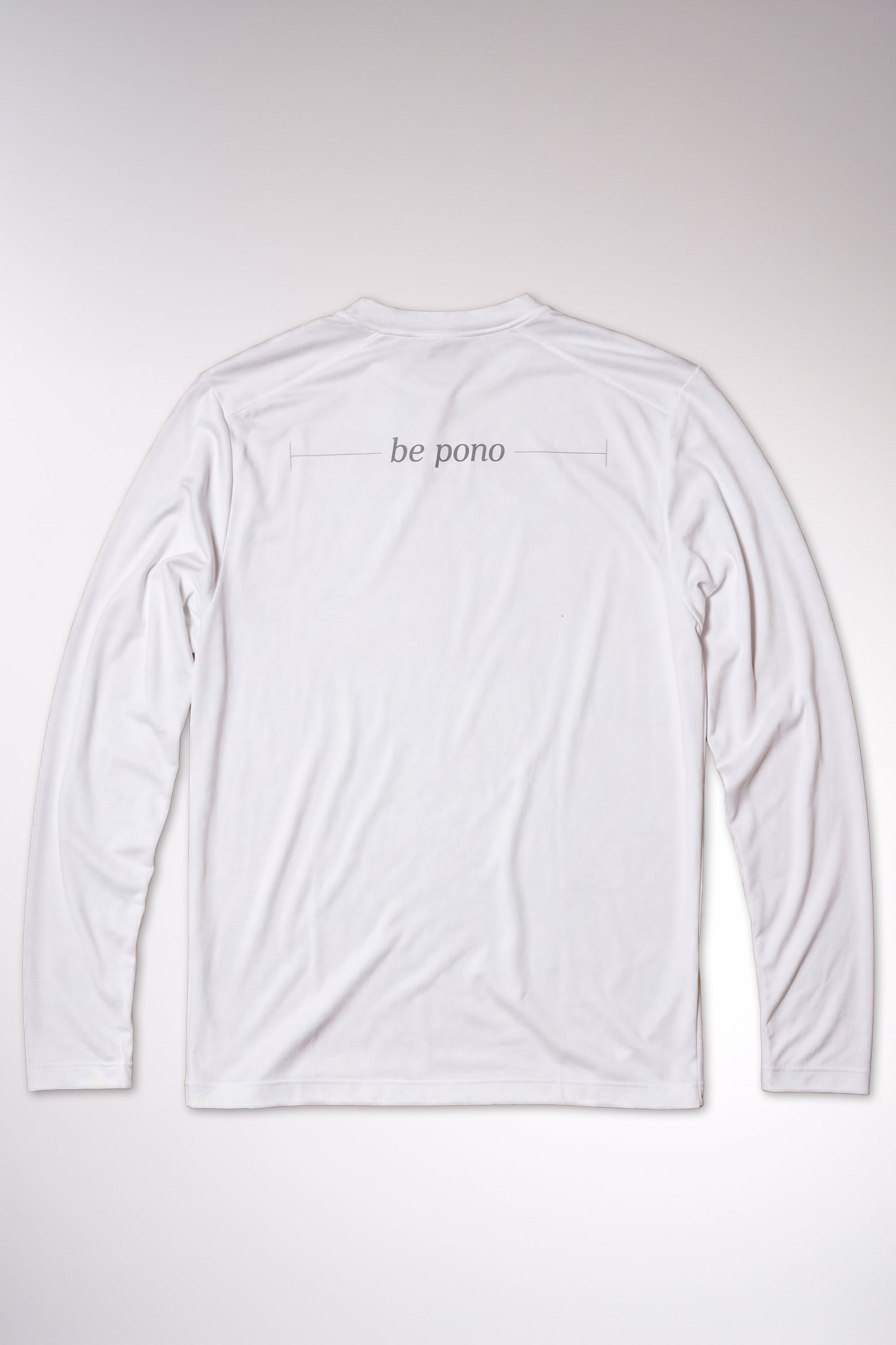 kailua hi surf tees be pono men's long sleeve upf 50 sunshirt in white – studio flat lay product shot of the back of the shirt. features the minimalist text be pono printed across the shoulders with clean horizontal accent lines, showcasing the relaxed performance fabric build and athletic crew neck against a neutral background