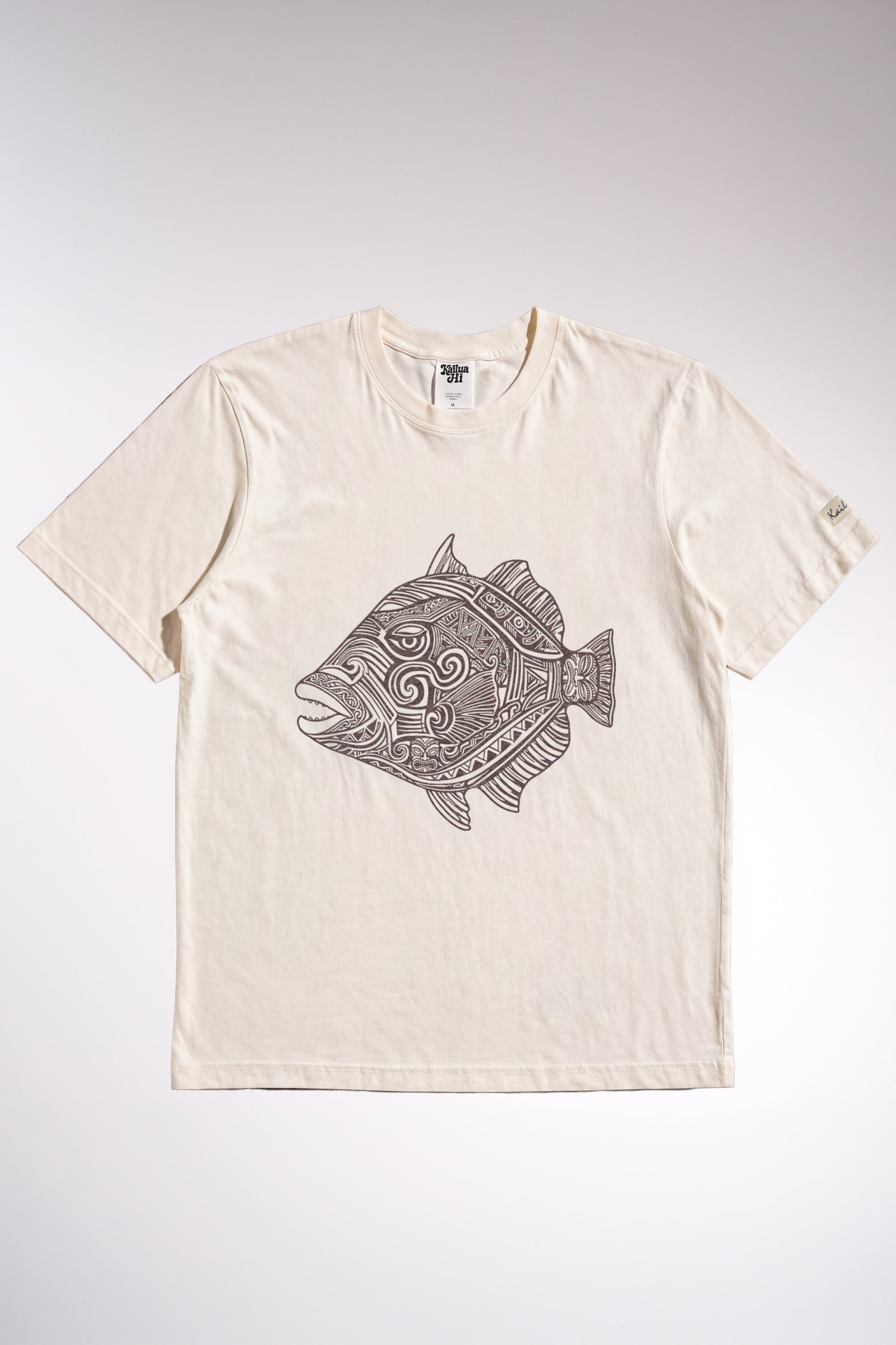 kailua hi surf tees humuhumu men's luxe tee in pearl brown – studio flat lay product shot showing the full front graphic. features a large brown intricate tribal woodcut style illustration of a humuhumu fish with swirling geometric patterns. includes a relaxed crew neckline, interior kailua hi woven neck label, and custom sleeve tag against a neutral background