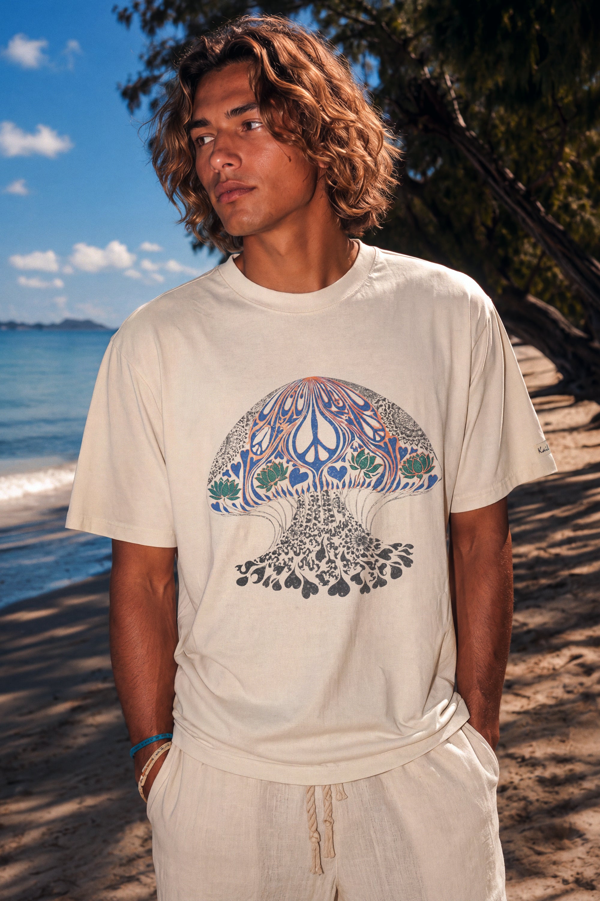 kailua hi surf tees psychedelic moon jelly luxe men's tee in faded ecru – waist-up close up lifestyle beach shot of a model showcasing the detailed jellyfish graphic print, relaxed crew neckline, and sleeve tag fit