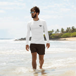 front view of white men’s rash guard with small chest mark; model walking at the waterline on a sunny beach
