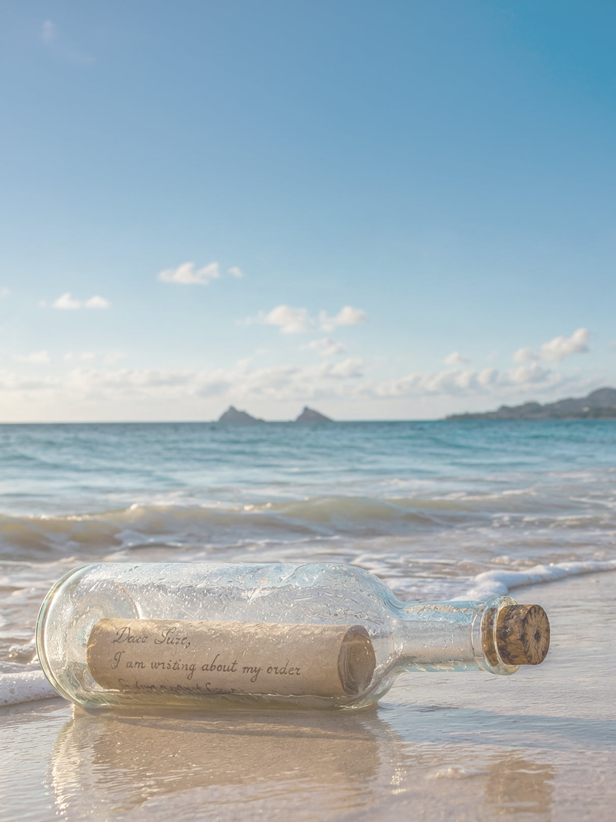 Glass bottle with a message on a beach with ocean and sky in the background