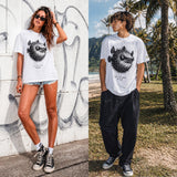 Two people wearing white t-shirts with a fish graphic design, one against a graffiti wall and the other outdoors.