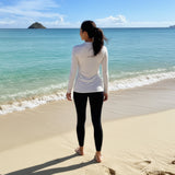 woman in white long-sleeve rash guard with “be pono” back print, standing at the Kailua shoreline facing the ocean