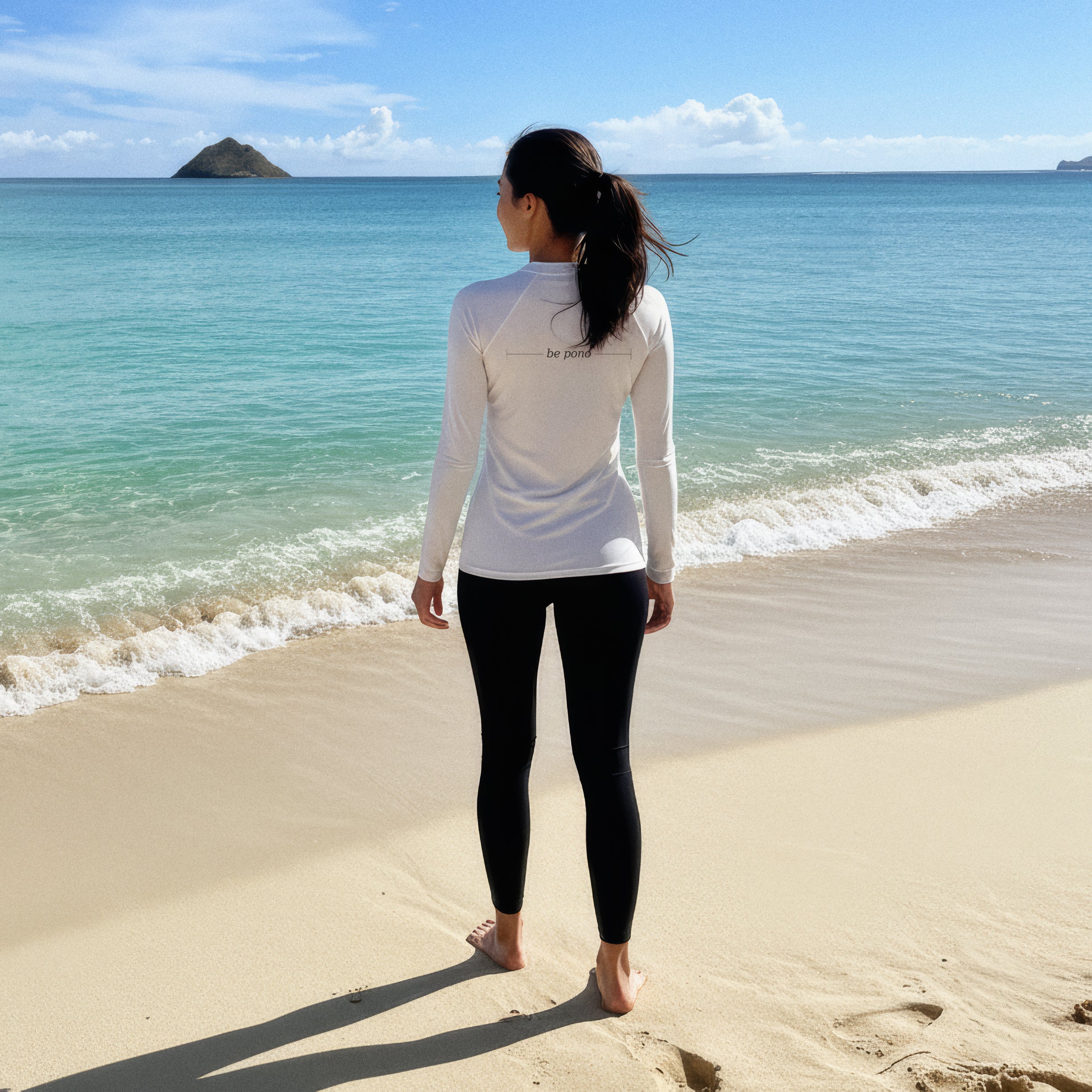 woman in white long-sleeve rash guard with “be pono” back print, standing at the Kailua shoreline facing the ocean